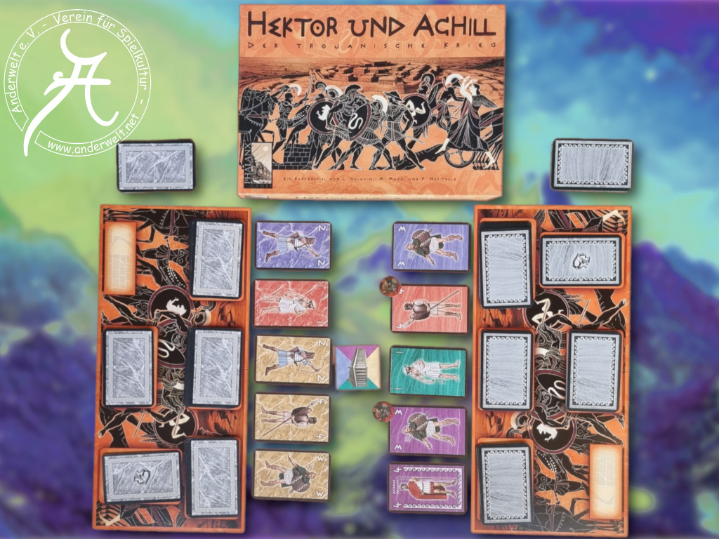 Die Spielschachtel zeigt altgriechische Kampfszenen. Davor breitet sich das Schlachtfeld nach zwei Seiten aus, auf dem verschiedene Kartenstapel und Kartenreihen aufmarschieren.