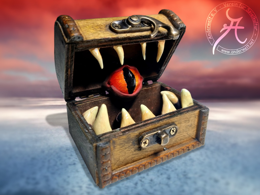 Zu sehen ist der mit sitzen Zähnen gesäumte Schlund der Mimik-Truhe, in dessen Mitte sich ein großes orangefarbenes Auge befindet.