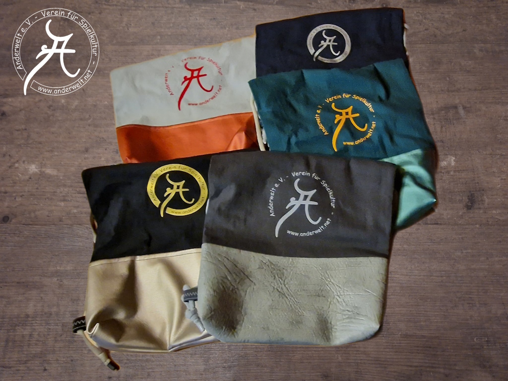 Das Bild zeigt fünf Rucksäcke mit Anderwelt-Logo, jeweils zweifarbig in verschiedenen Farbkombinationen ausgeführt (unten Kunstleder, oben Baumwolle).