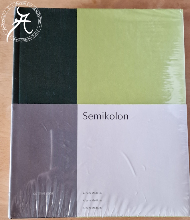 Das Bild zeigt die Vorderseite des shrinkwrap-verpackten Albums. Die untere Hälfte ist mit einer Papierbanderole mit der Produktbezeichnung bedeckt.