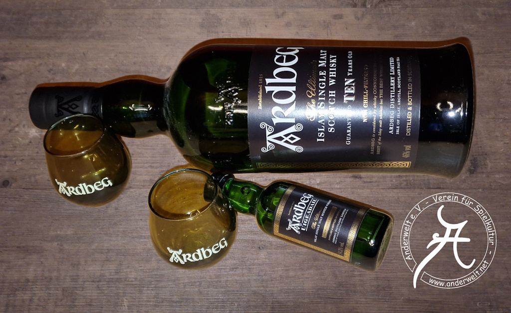 Das Bild zeigt eine horizontal liegende, dunkelgrüne Flasche Ardbeg TEN Whisky mit schwarzem Etikett sowie weißer und goldener Aufschrift. Links davor stehen zwei hellbraune, stiellose Nosing-Gläschen mit weißer Ardbeg-Aufschrift. Rechts daneben liegt ein dunkelgrünes Probierfläschchen Ardbeg Uigeadail Whisky.