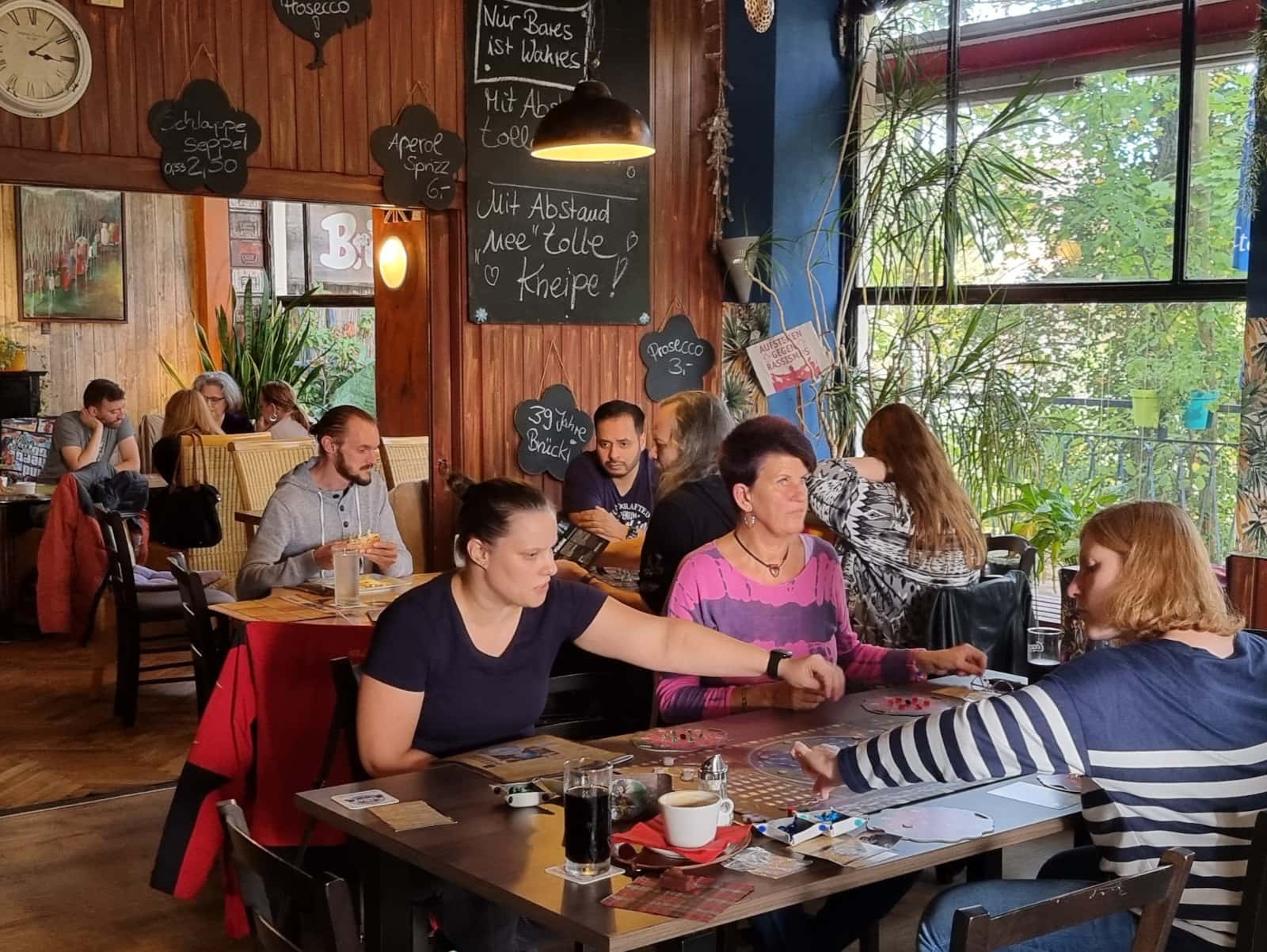 Mehrere Tische mit verschiedenen Spielrunden. Wenn die Spieler angestrengt schauen, dann bestimmt wegen der Mühe beim Spiel-Aufbau und den Regelerklärungen.