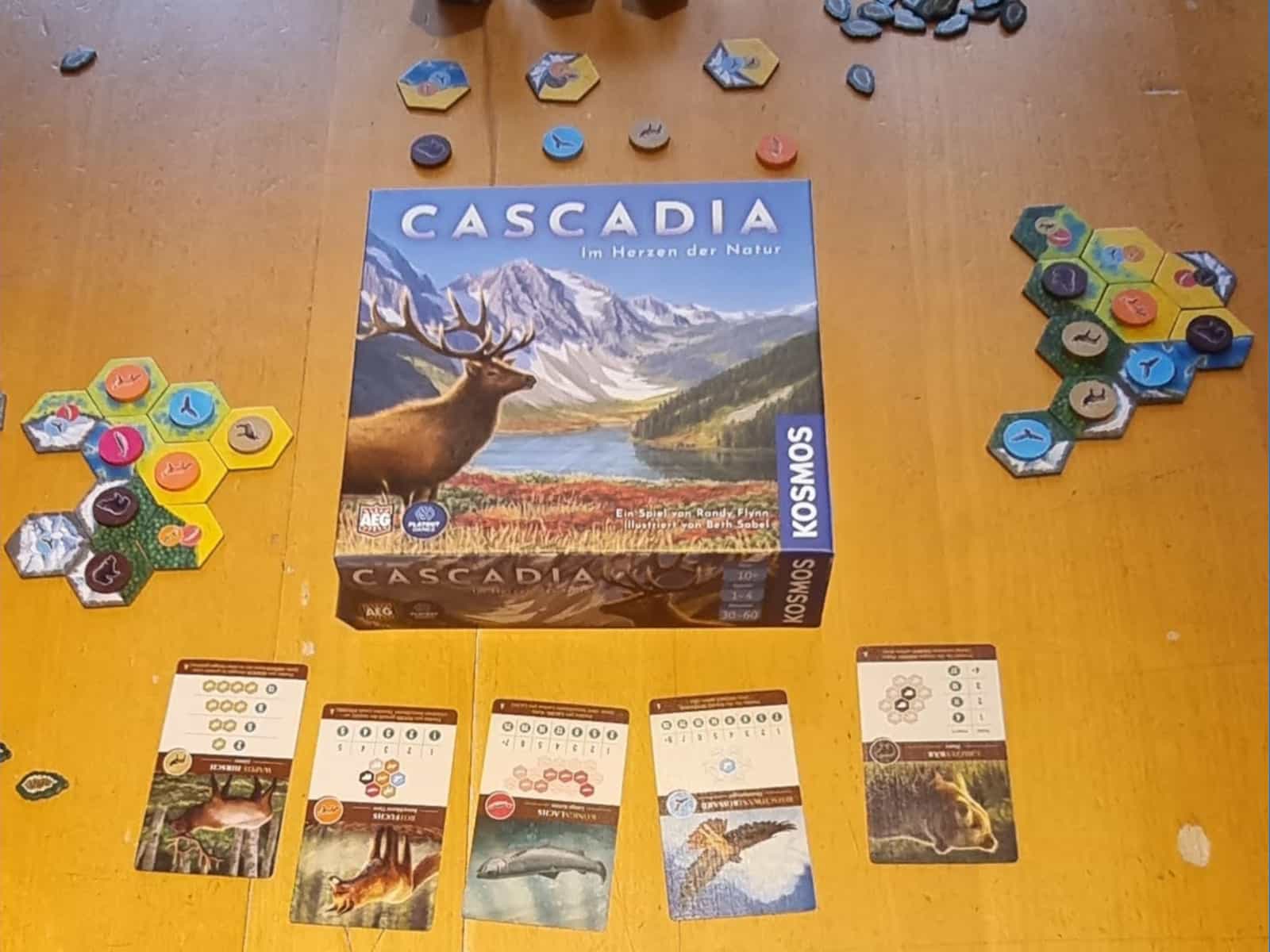 Spiele-Schachtel von Cascadia mit Landschafts-Plättchen und Wertungskarten drumherum.