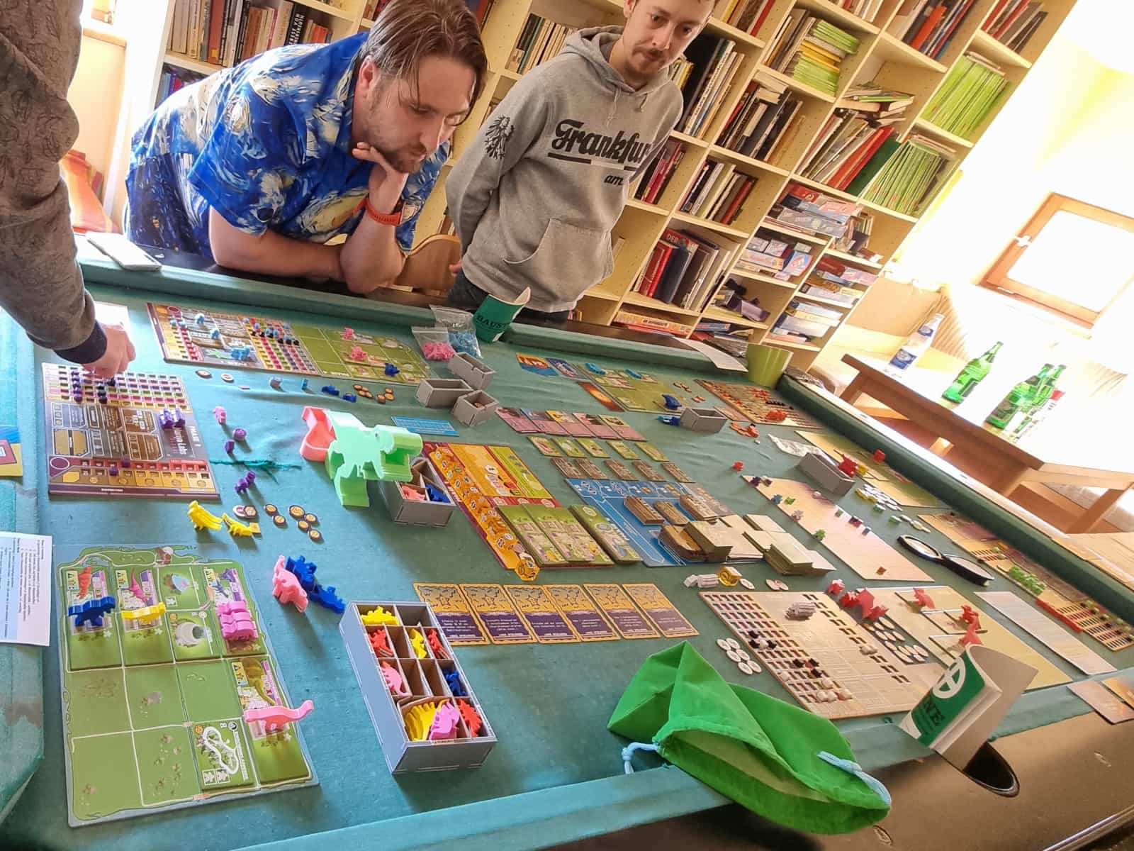 Spielrunde Dinosaur Island auf einem Billard-Tisch ausgebreitet, mit konzentrierten Spielern drumherum.