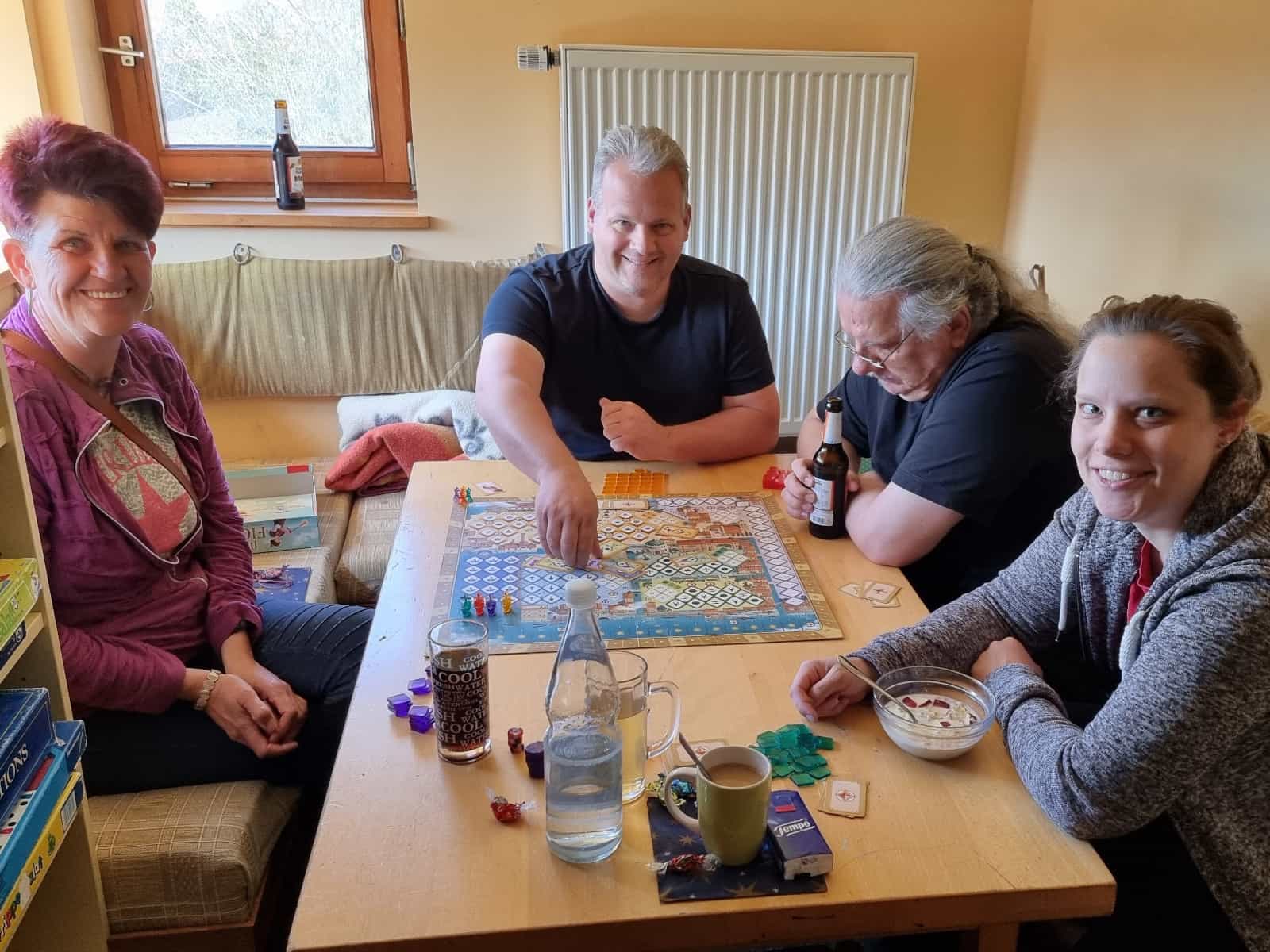 Alle sitzen lachend um den Tisch herum bei einer gemütlichen Spielrunde Mille Fiori.