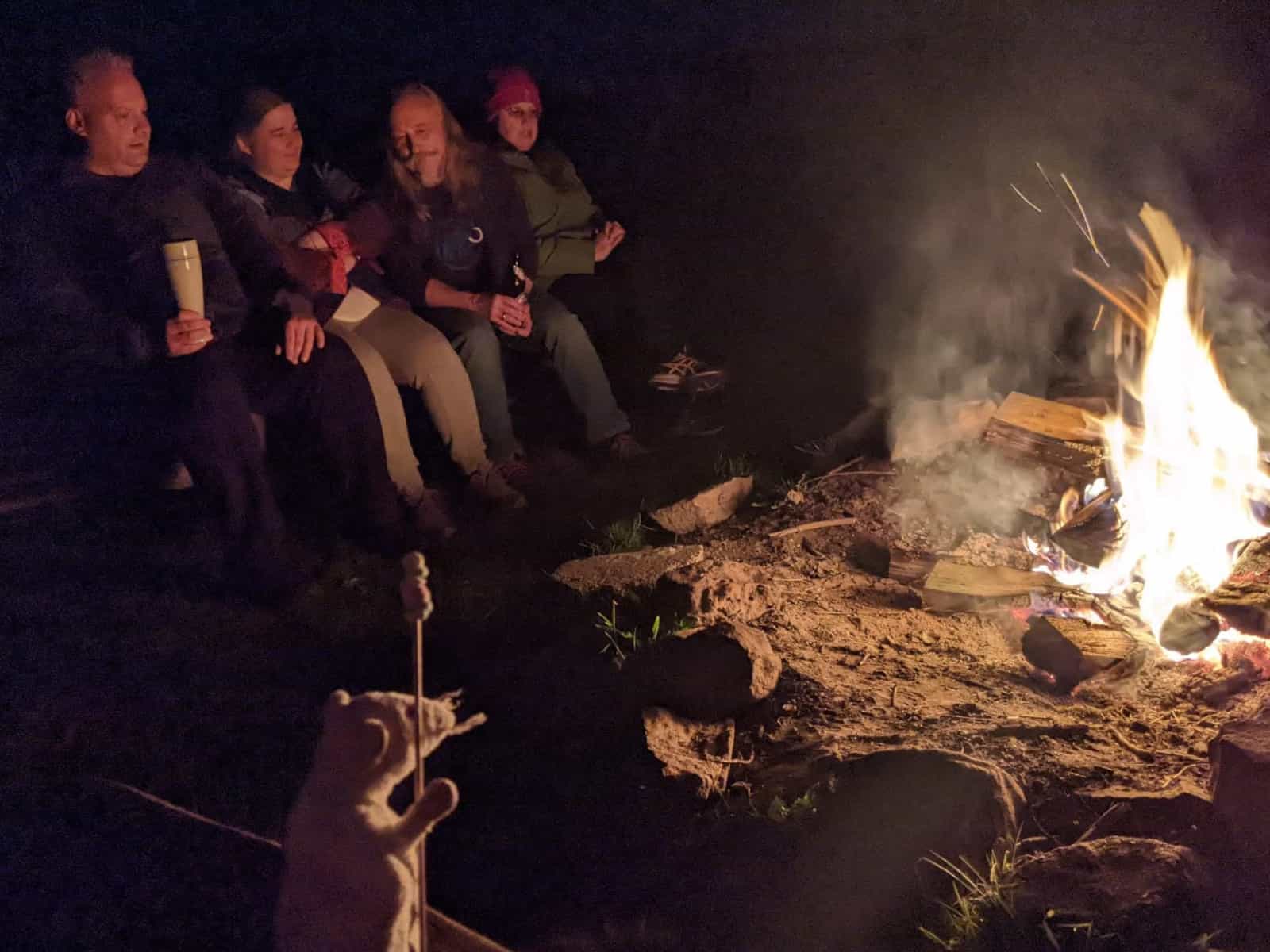 Gesellige Runde am nächtlichen Lagerfeuer und im Vordergrund eine kleine Plüsch-Maus mit bunten Mini-Marshmallows.