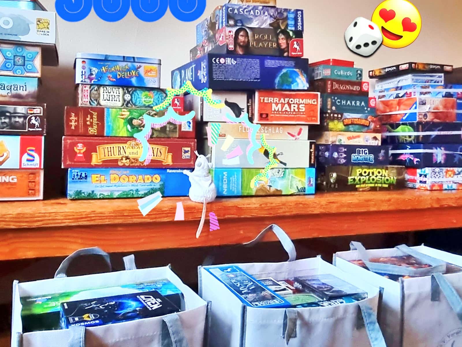 Aufgetürmte Spiele-Schachteln und davor drei Anderwelt-Tüten mit weiteren Spiele-Schachteln darin und eine erstaunte Plüsch-Maus.