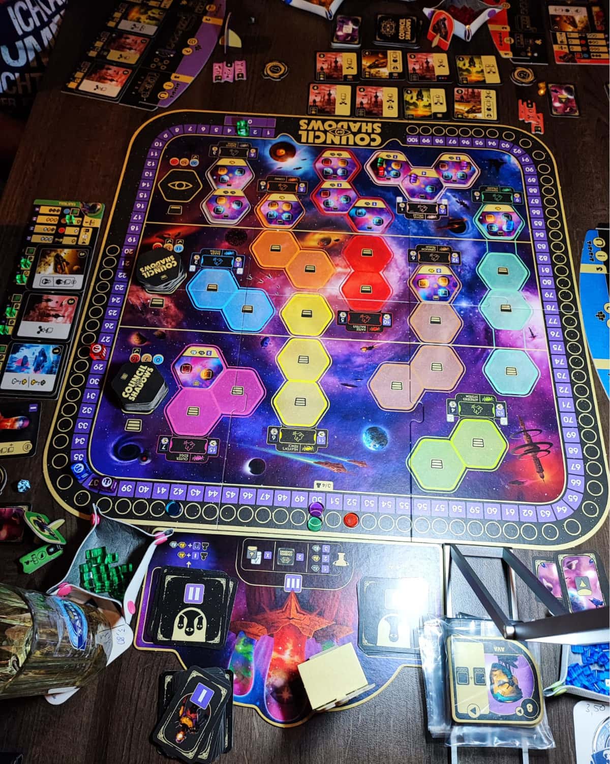 Zu sehen ist ein Tisch mit großem Spielbrett und weiterem Spielmaterial wie Karten, Plättchen und persönlichen Spielplänen.