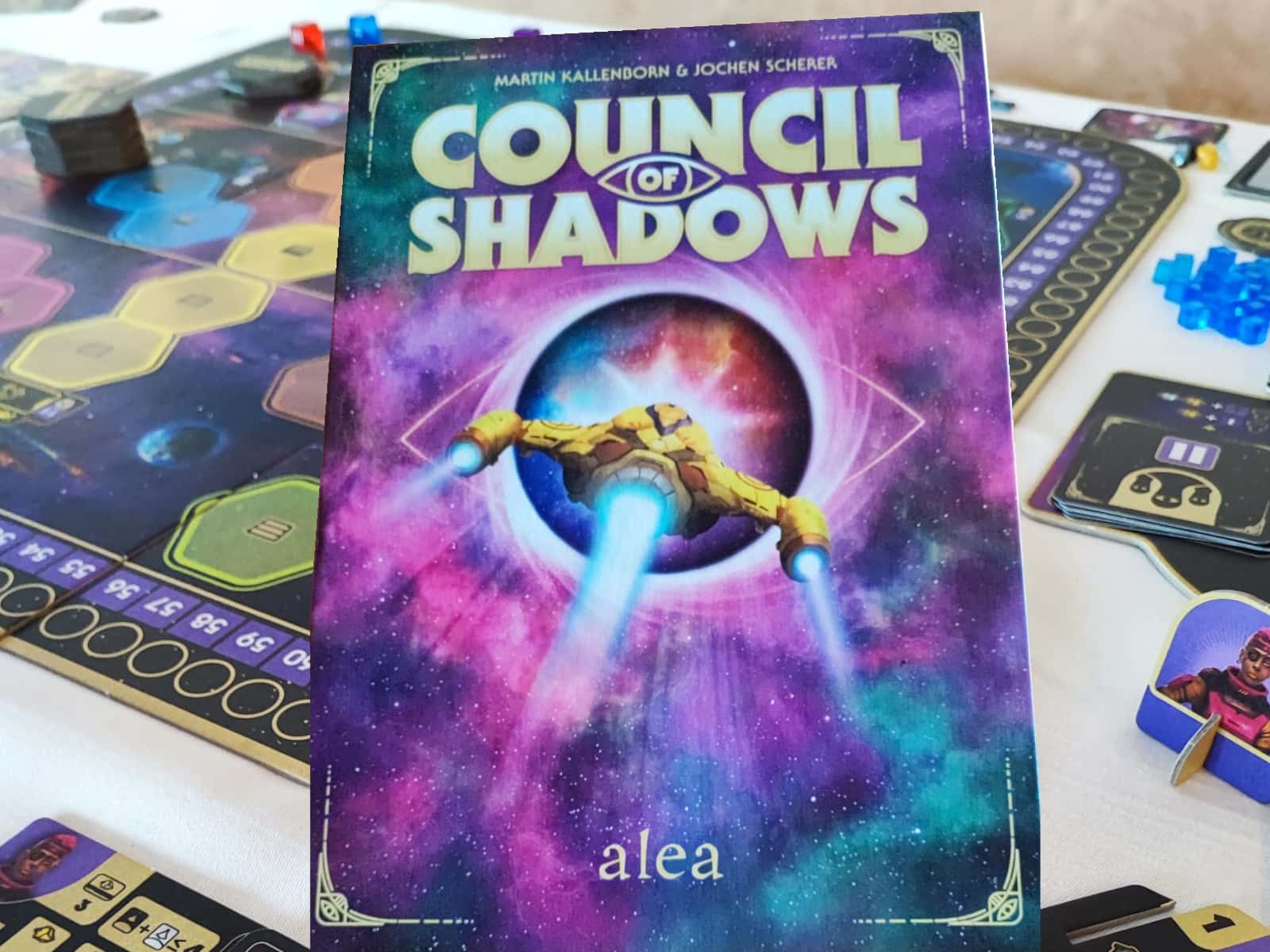 Zu sehen ist die Spiele-Schachtel mit ewinem Raumschiff, das in einer Art "schwarzem Loch" verschiwndet. Im Hintergrund leicht unscharf der Spielplan mit weiterem Spielmaterial.