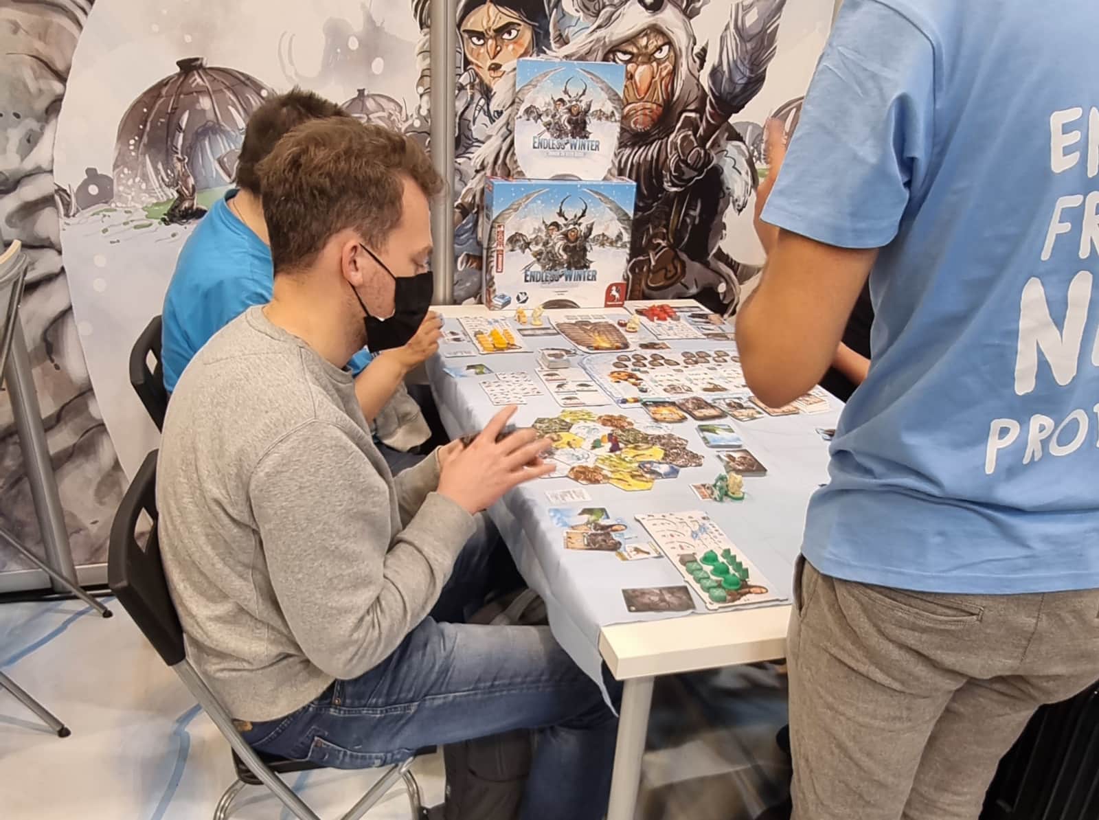 Eine Spielrunde Endless Winter. Der Tisch ist komplett belegt mit Spielplänen, Karten und Plätchen.