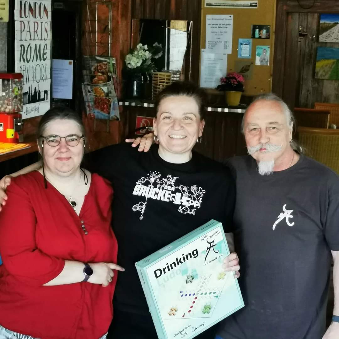 Die erste Vorsitzende vom Anderwelt e.V. überreicht dem Vorstand des Brückenkopfes ein Spiel als Präsent und Dankeschön für die letzten erfolgreichen 15 Stammtisch-Jahre. Von links nach rechts: Nicole, Milena, Gerhard.