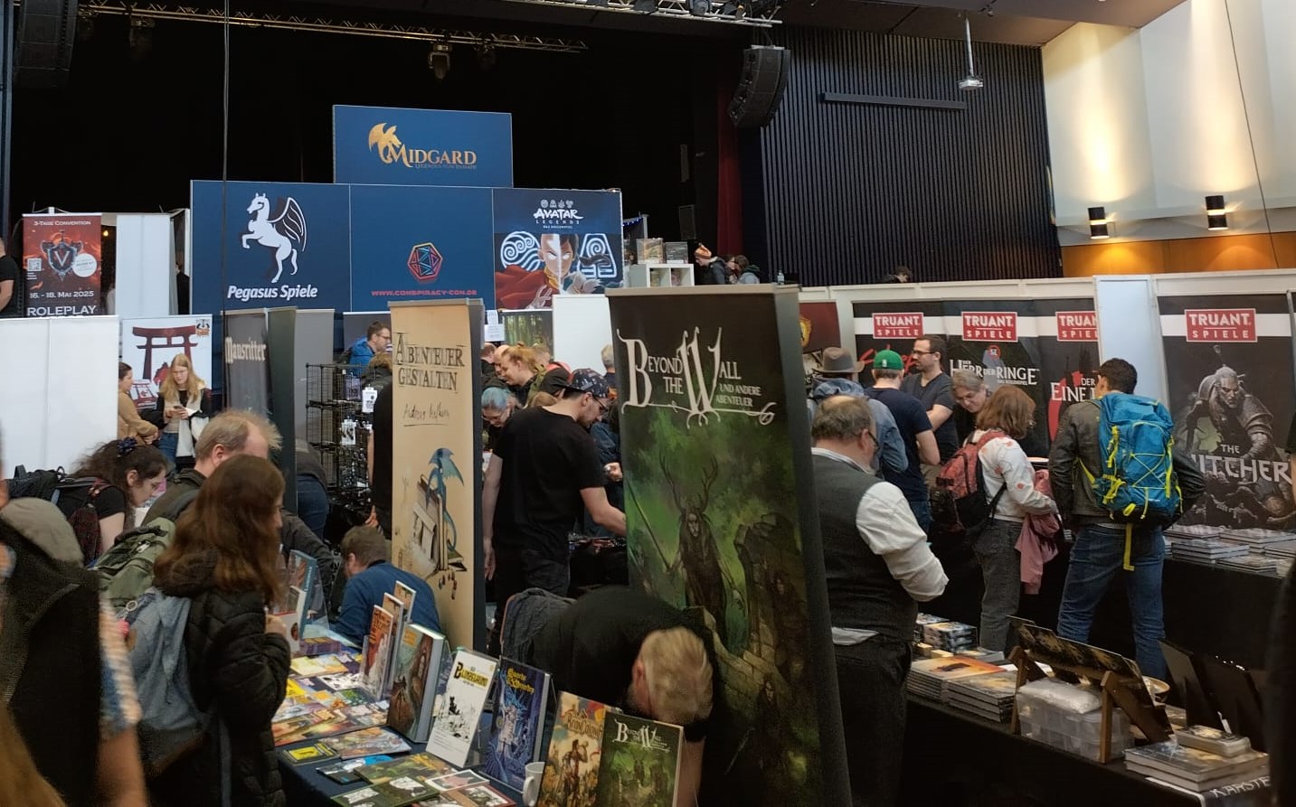 Messe-Halle mit dichten Ständen und vielen Besuchern. Angeboten werden Materialien zu verschiedenen Rollenspielen.