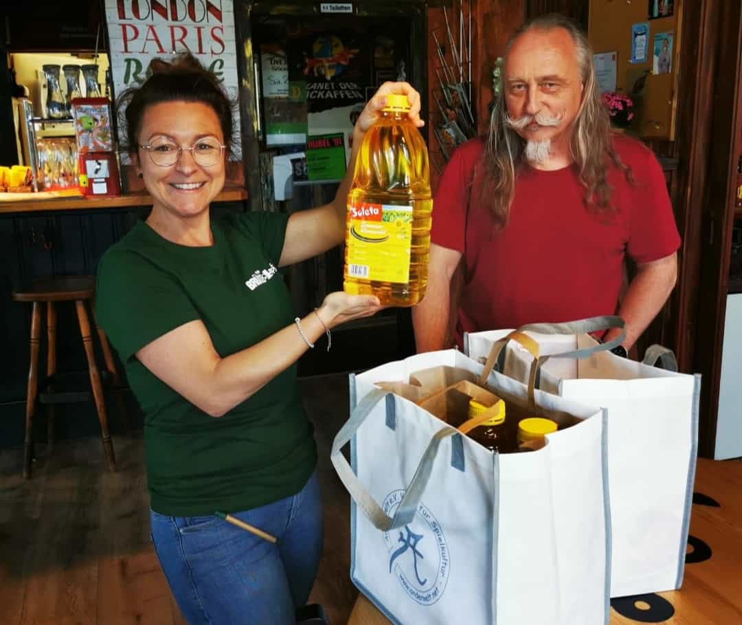 Ein Brückenkopf-Mitglied hält hält strahlend eine gespendete Flasche Sonnenblumen-Öl hoch.