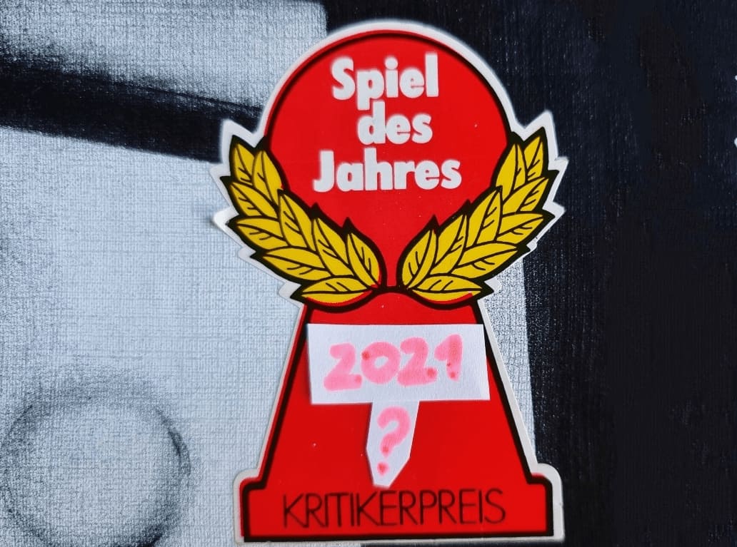 Berühmtes Logo des Kritikerpreises "Spiel des Jahres" in dessen Mitte handschriftlich "2021?" geschrieben wurde.