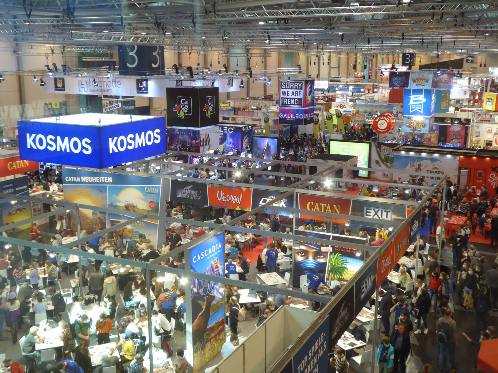 Zu sehen ist Messehalle 3 der SPIEL-Messe 2022 mit Blick von oben auf die vielen Stände und Besucher.
