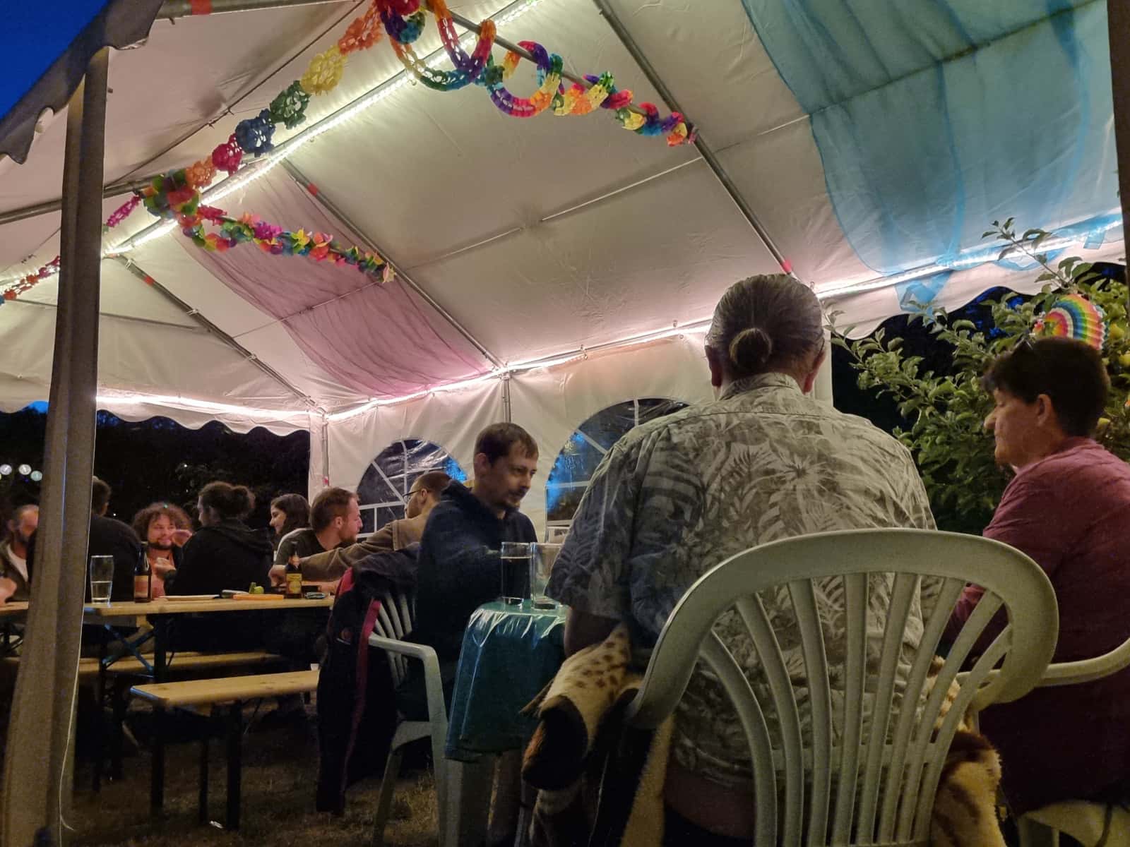 Viele Besucher, die es sich unter dem beleuchtetem Festzelt auf den Bierbank-Garnituren gemütlich gemacht haben, sich unterhalten und vereinzelt auch Spiele spielen.